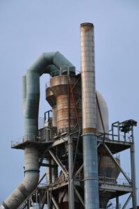Industrial air cannon mounted on a bulk material hopper beside a conveyor in a working facility.
