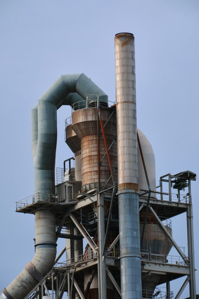 Industrial air cannon mounted on a bulk material hopper beside a conveyor in a working facility.